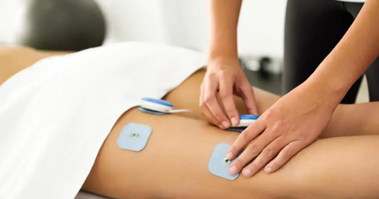Elektrostymulacja efekty po 10 zabiegach. Terapeuta umieszcza elektrody na udzie pacjenta, przygotowując do kolejnego zabiegu.